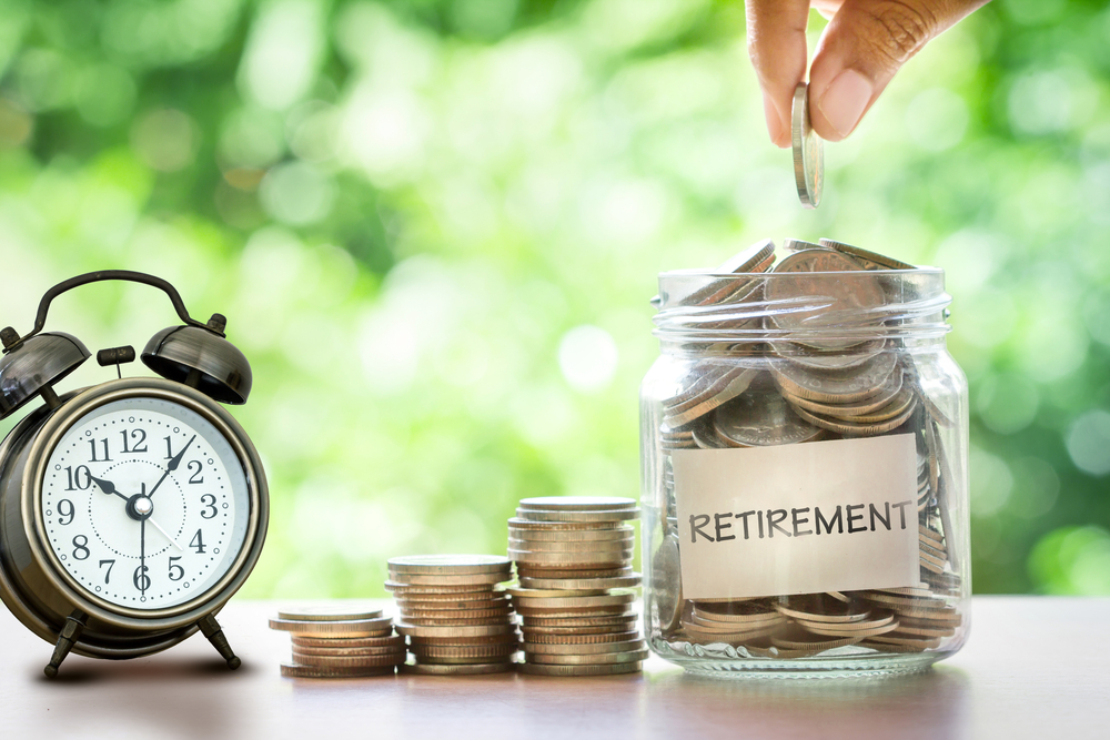 hand putting a coin into a jar labeled retirement, next to an alarm clock