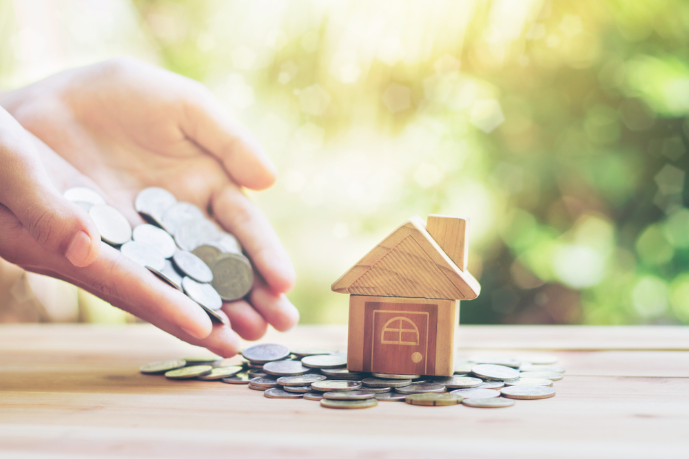 small wooden house with a hand full of coins