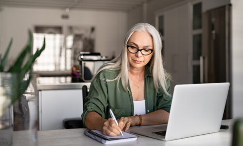Senior,Stylish,Woman,Taking,Notes,In,Notebook,While,Using,Laptop