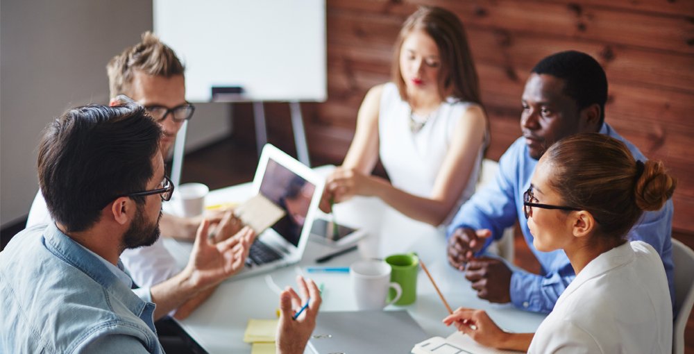 image shows a group of people sat around a table talking