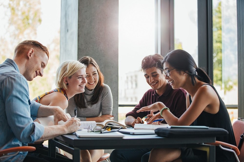 young people sitting around a table with books, pens, and calculators