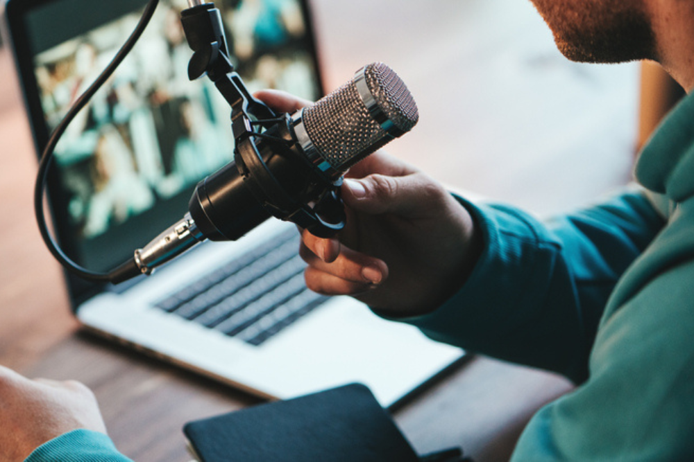 A man is using his laptop and professional microphone in a presentation/podcast set up.