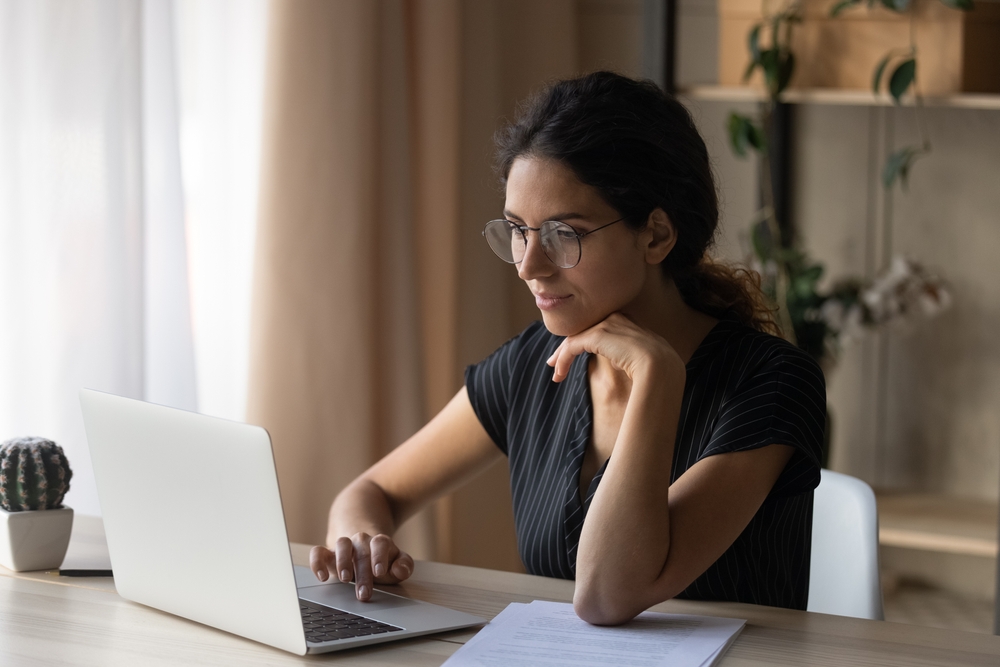 A young hispanic woman is sat at her laptop, doing work.